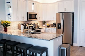 A modern kitchen with white cabinets, a stainless steel refrigerator, a microwave, and a granite countertop. - Reel It Inn is a 3/2 home in St James City. 3 kayaks,dock space, hottub, 2 bikes (Saint James City)