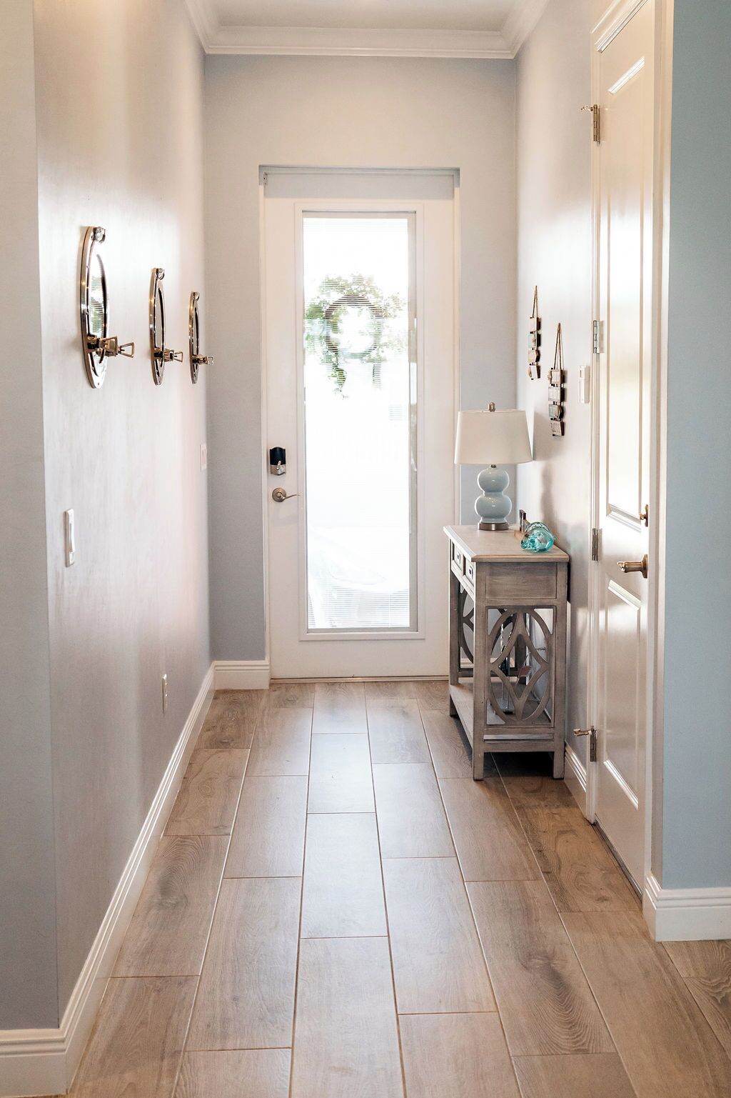 A hallway with a wooden floor, a door at the end, and a small table with a lamp.