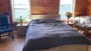 Une pièce de cabane en bois comprenant un lit, une chaise, une table de chevet et une fenêtre donnant sur l’eau.