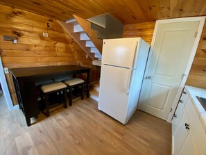 A compact kitchen with a wooden interior, a white refrigerator, a bench, and a staircase.