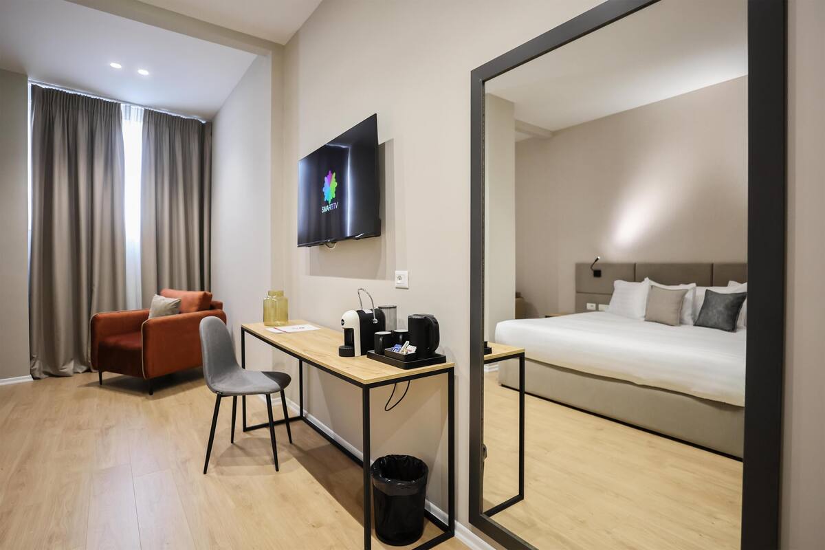 Quarto de hotel com cama, escrivaninha com cadeira, televisão e janela com cortinas.