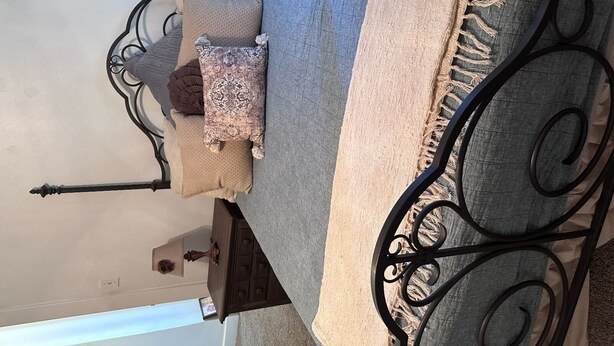 A bed with a metal frame, multiple pillows, a beige throw blanket, and a dark wooden nightstand.