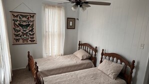 A bedroom with two wooden beds, a ceiling fan, a window with sheer curtains, and a butterfly wall art.