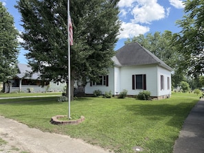 A small white house with a dark roof, surrounded by a well-maintained lawn and trees.