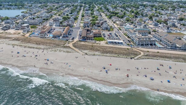 Vue aérienne d’une ville côtière avec une plage, des maisons et un port de plaisance.