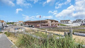 Un hôtel situé en bord de mer, doté d’une promenade, d’un mât avec un drapeau et d’un parking.