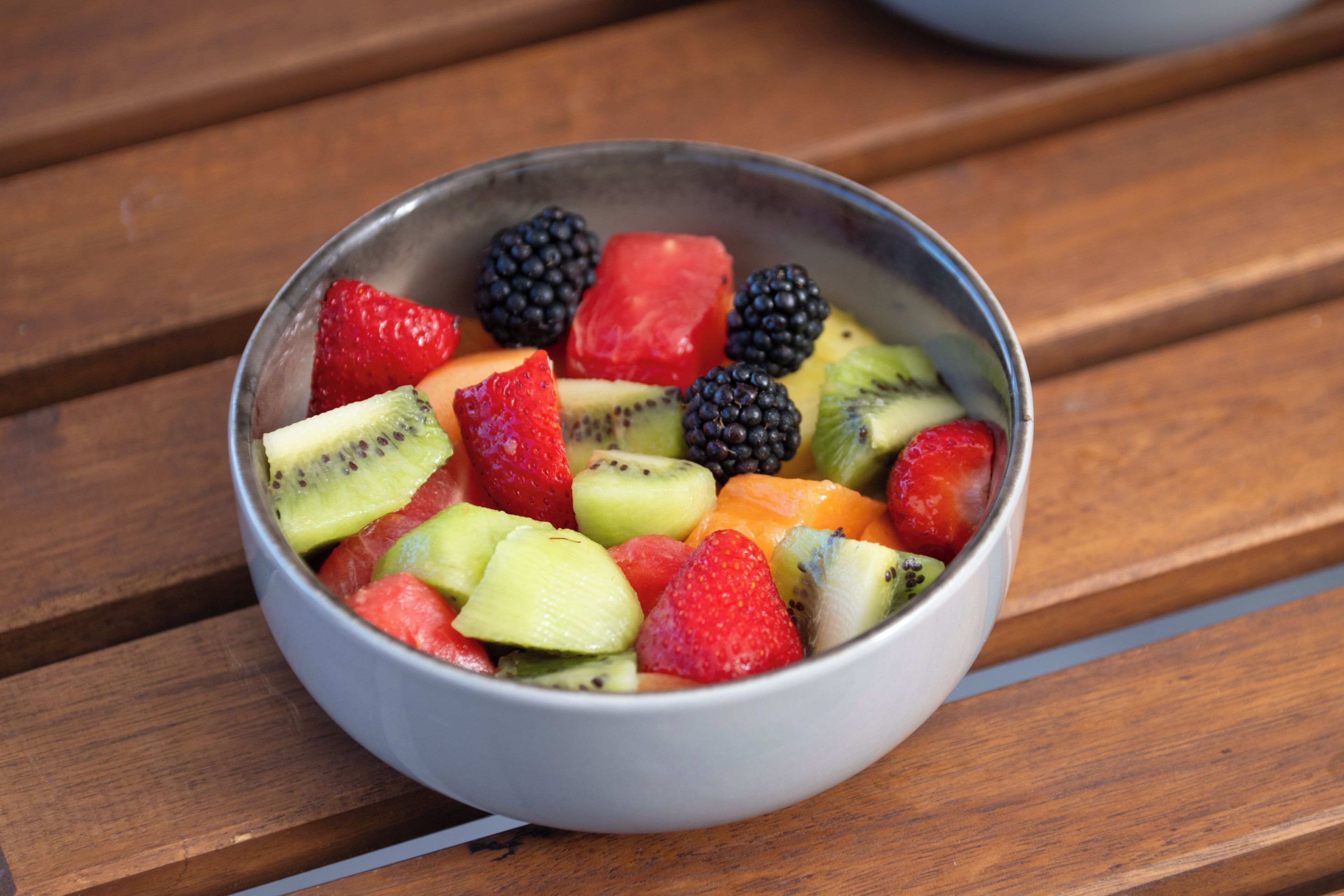 A bowl of assorted fruits on a wooden surface.