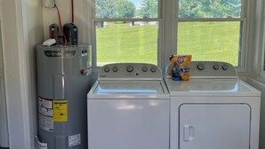 Une buanderie équipée d’un lave-linge et d’un sèche-linge, d’un chauffe-eau et d’une fenêtre donnant sur une cour verdoyante.
