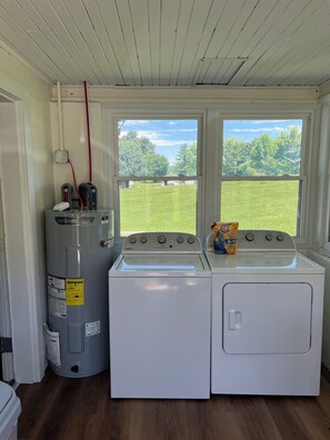 Ein Waschraum mit Waschmaschine und Trockner, einem Warmwasserbereiter und einem Fenster mit Blick auf einen Rasen.