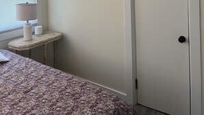 Une chambre dotée d’un ventilateur de plafond, d’un lit recouvert d’une couvre-lit à motifs, d’une table de chevet avec une lampe et d’une fenêtre avec des stores.