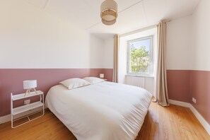 Une chambre à coucher comprenant un lit, une table de chevet, une lampe, une fenêtre avec des rideaux et un luminaire au plafond.