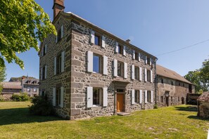 A stone building with a central entrance, multiple windows, and a surrounding grassy area. - Le Domaine du Rocher - Pour 12 avec grand jardin (Neussargues-Moissac)