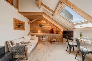 A loft-style room with a wooden ceiling, a dining area with a table and chairs, and a cozy seating area with a sofa and cushions. - Cabane Malou avec jardin et à  200m des pistes (La Salle-les-Alpes)