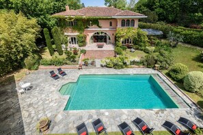 Une grande maison avec une piscine, une terrasse en pierre et un espace salon extérieur.