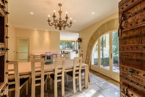 Un espace repas avec une table et des chaises en bois, un lustre et une vue sur une terrasse extérieure, accessible par une porte vitrée.