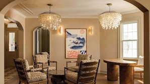 Ein Zimmer mit einem runden Tisch, gemusterten Stühlen, einer Chandelierleuchtre und einem gerahmten Poster an der Wand.