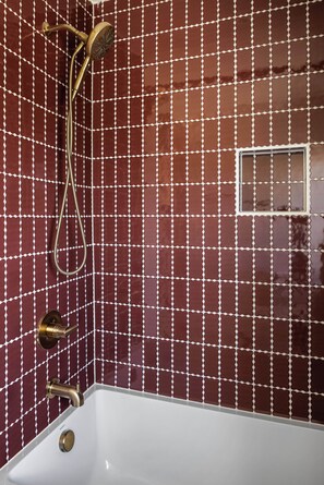 A bathroom with a white bathtub, a shower with a handheld showerhead, and a wall with a grid pattern of red tiles.