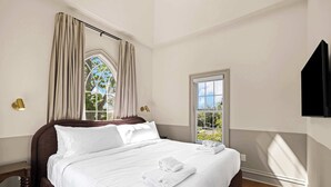 Ein Hotelzimmer mit einem großen Bett, einem Fenster mit Vorhängen, einem Flachbildfernseher und einem Nachttisch.