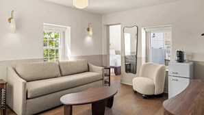Ein modernes Hotelzimmer mit Sofa, Ohrensessel, Holz-Couchtisch und Schrank.