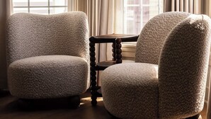 A room with two upholstered chairs, a hanging light fixture, and a window with curtains.