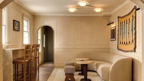 A room with a curved sofa, a small round table, a wooden stool, and a patterned rug.