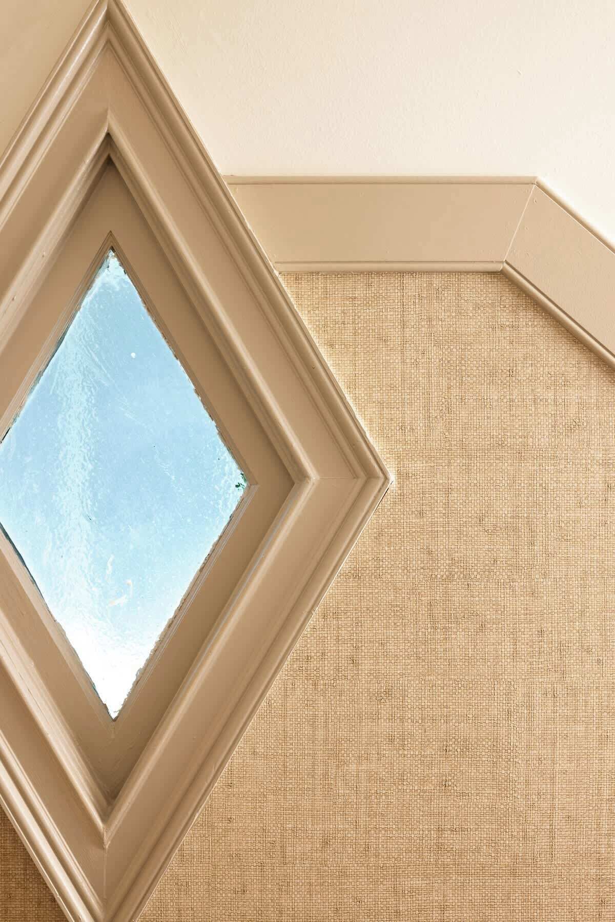 Eine Ecke eines Raumes mit einer strukturierten, beige farbenen Wand, einem Fenster mit freiem Ausblick und einer Eckleiste.