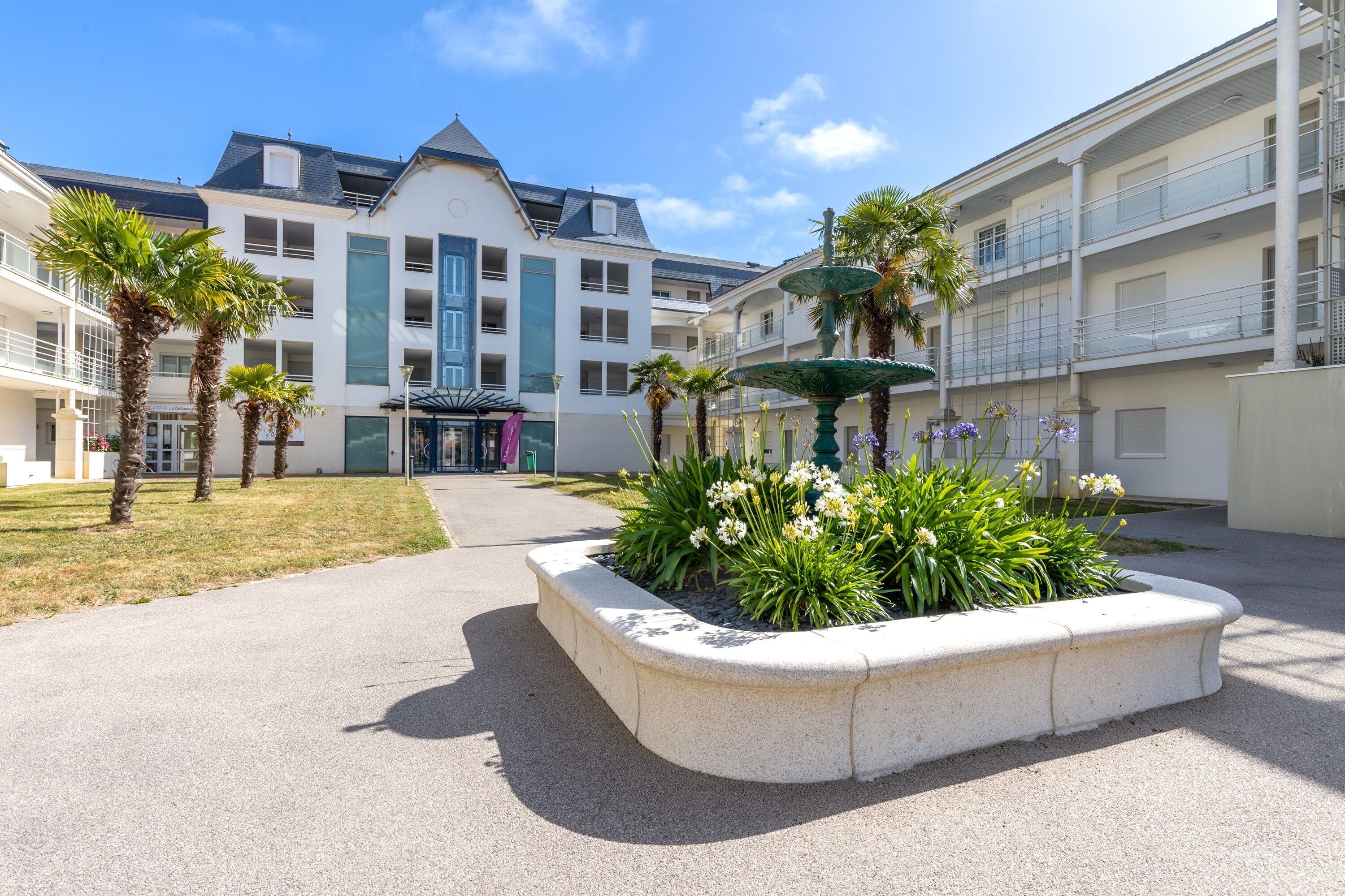 A courtyard with a fountain, palm trees, and a building with balconies.