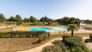 A swimming pool with a wooden deck, surrounded by greenery and a clear sky. - Green Flat - Appt proche des Sables d'Olonnes (L'Aiguillon-sur-Vie)
