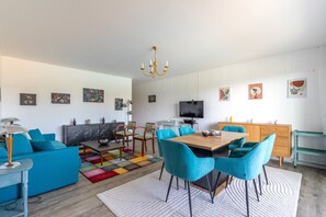 Ein modernes Wohnzimmer mit einer Couch, Sesseln, einem Esstisch, einem Fernseher und Kunstwerken an den Wänden.