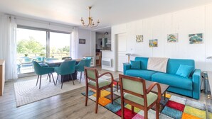 A modern living room with a blue sofa, wooden chairs, a dining table, and a colorful rug. - Green Flat - Appt proche des Sables d'Olonnes (L'Aiguillon-sur-Vie)