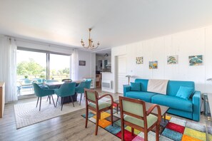 Ein modernes Wohnzimmer mit einem blauen Sofa, Holzstühlen, einem Esstisch und einem farbenfrohen Teppich.