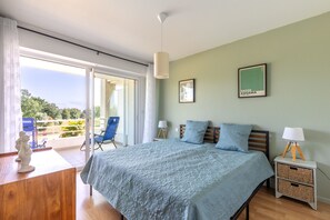 Ein Schlafzimmer mit Bett, Nachttisch, Lampe, Stuhl und Blick ins Freie.
