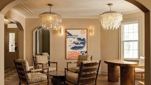 A room with a round table, patterned chairs, a chandelier, and a framed poster on the wall.