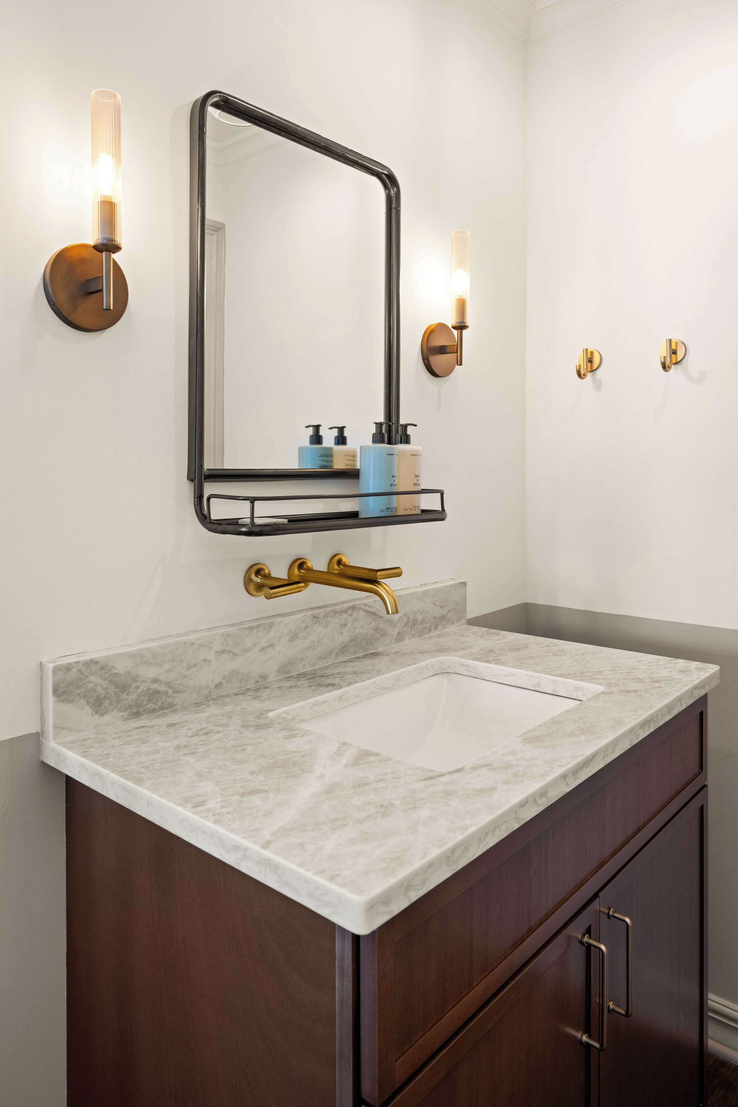 A bathroom with a marble sink, gold fixtures, and wall-mounted sconces.