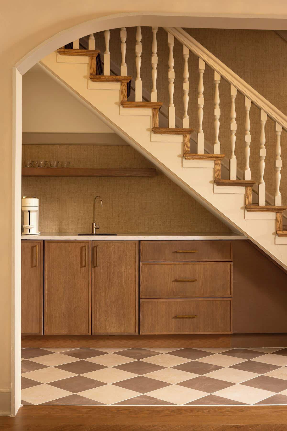 Une cuisine avec des meubles de rangement en bois, un évier et un escalier doté de balustrades blanches.