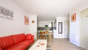 Um apartamento moderno com sofá vermelho, mesa de jantar com cadeiras, cozinha e sala de estar.