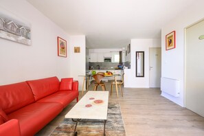 Eine moderne Wohnung mit einem roten Sofa, einem Esstisch mit Stühlen, einer Küchenzeile und einem Wohnbereich.