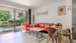 Uma sala de estar moderna com porta de vidro que dá para uma área externa, um sofá vermelho, uma mesa de centro e uma mesa de jantar com cadeiras.