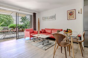 Ein modernes Wohnzimmer mit Glastür zum Außenbereich, einem roten Sofa, einem Couchtisch und einem Esstisch mit Stühlen.