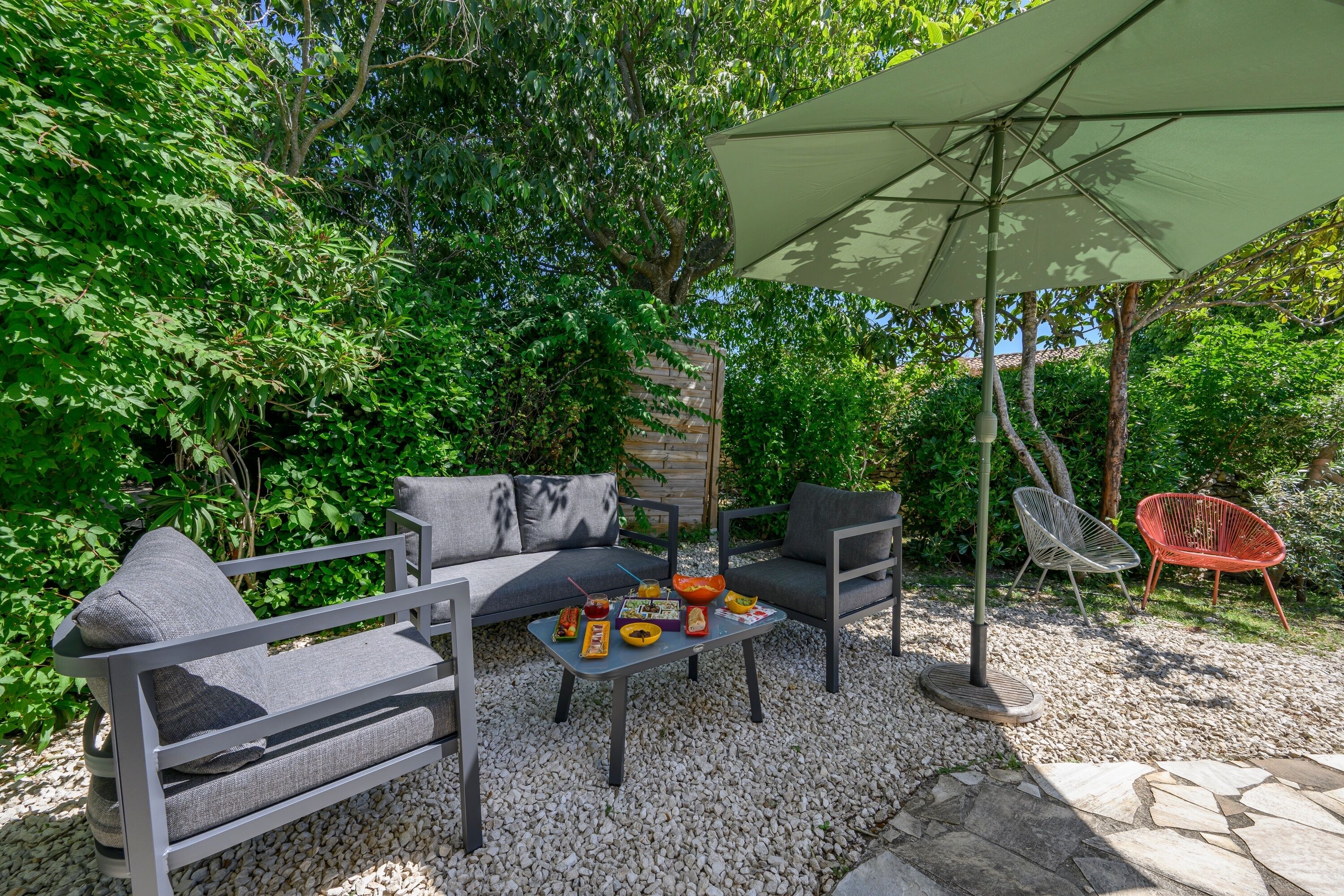 An outdoor seating area with a sofa, chairs, a table, and an umbrella.