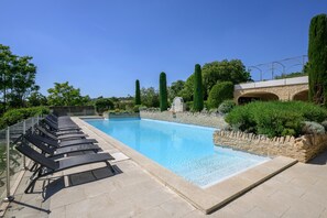 Ein Swimmingpool mit Liegestühlen, Steinmauern und einer Steinbrücke.