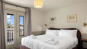 Una camera d'albergo con un letto grande, un balcone con tende, una lampada a parete e due quadri appesi.