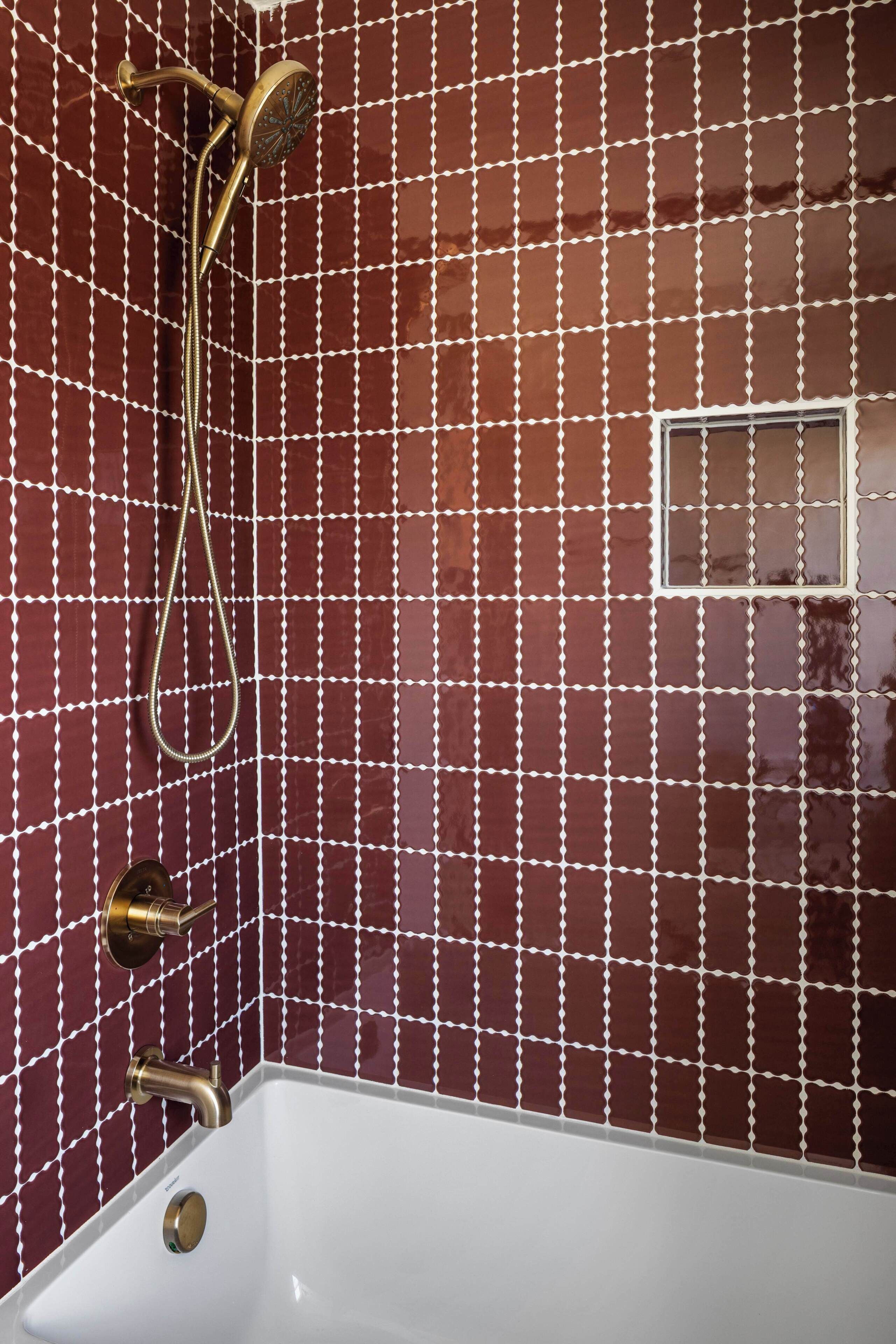 A bathroom with a white bathtub, a shower with a handheld showerhead, and a wall with a grid pattern of red tiles.