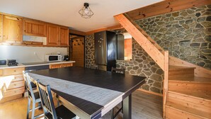 A modern kitchen with wooden cabinets, a large dining table, a stone accent wall, and a wooden staircase. - Le Pré de l'Arche - À 400 m des télécabines (Oz)