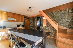 Eine moderne Küche mit Holzausbau, einem großen Esstisch, einer Wand mit Steinakzenten und einer Holztreppe.
