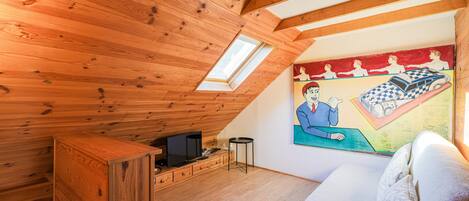 A room with wooden ceiling beams, a television, a small table, and a painting on the wall.