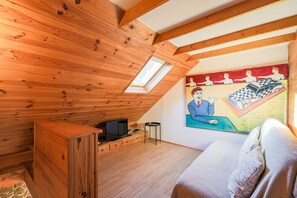 Een kamer met houten balken in het plafond, een televisie, een tafeltje en een schilderij aan de muur.
