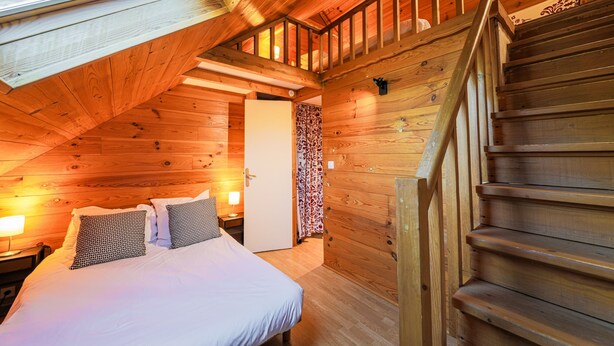A wooden interior with a bed, a nightstand, a lamp, a staircase, and a door leading to another room. - Le Pré de l'Arche - À 400 m des télécabines (Oz)