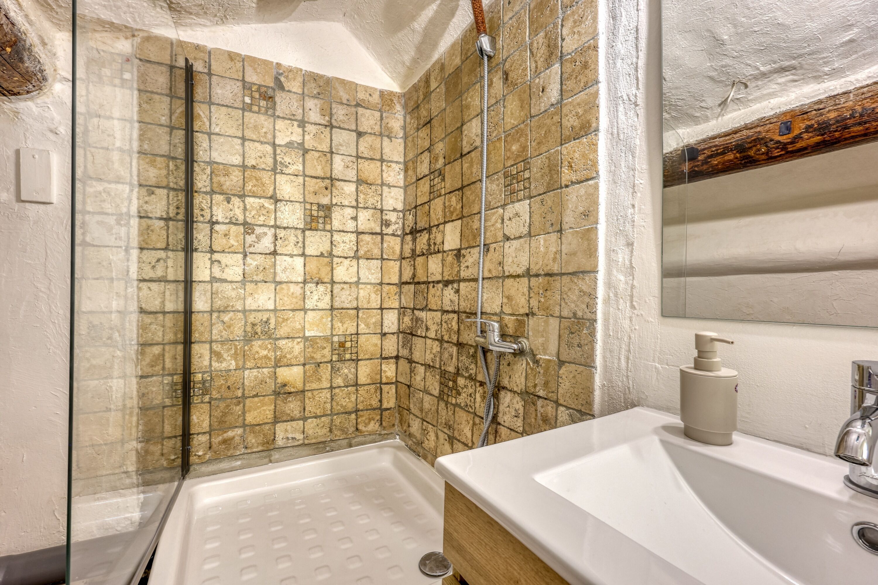 Une salle de bain avec une douche à parois de verre, un lavabo blanc et un meuble-lavabo en bois.