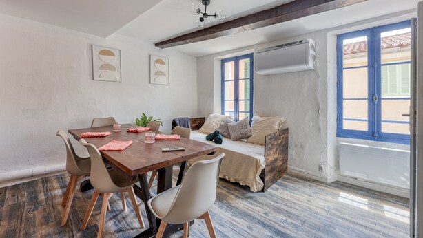 Una stanza con un tavolo da pranzo in legno, sedie bianche, un divano e una finestra con persiane blu.